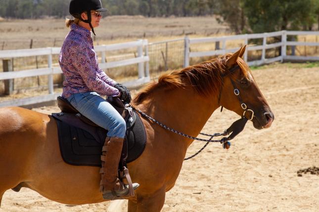 Woman riding light brown horse.