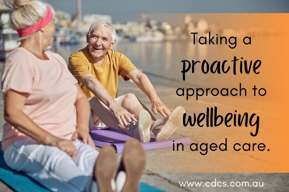 A senior man and senior woman practicing yoga by the water. Text reads: Taking a proactive approach to wellbeing in aged care.