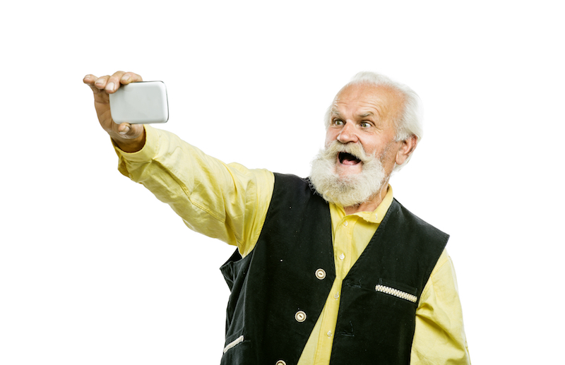Old active bearded man taking selfie with mobile phone isolated on white background